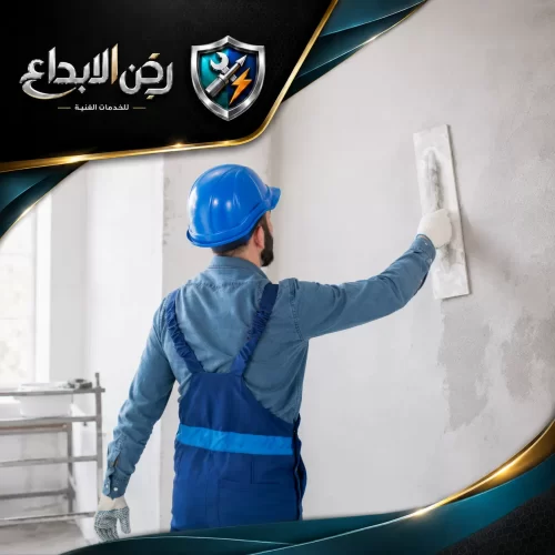 عامل يرتدي خوذة زرقاء يقوم بتسوية الجدران وتنعيمها بمهارة، لضمان جودة أعمال المحارة والدهانات.