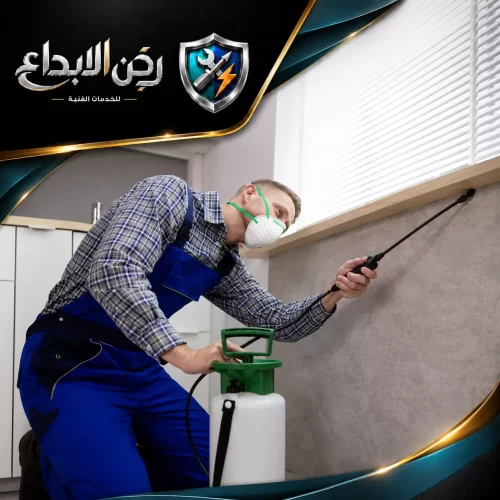 شركة رش المبيدات في دبي 0553689103 ركن الابداع فني يرتدي قناعاً واقياً وملابس عمل ويرش الحواف السفلية للجدران والنوافذ ضمن أعمال رش الحشرات المنزلية